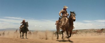 Movie still from “The Cowboys” (1972), directed by Mark Rydell – A man on a horse running in the dirt; Wide shot, Low angle