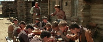 Movie still from “The Cowboys” (1972), directed by Mark Rydell – A group of people sitting around a table eating food; Medium shot, High angle