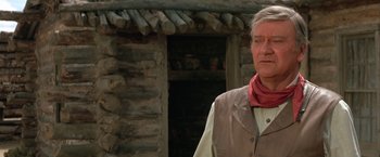 Movie still from “The Cowboys” (1972), directed by Mark Rydell – A man in a cowboy outfit standing in front of a log cabin; Close Up shot, Low angle