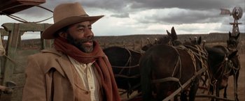 Movie still from “The Cowboys” (1972), directed by Mark Rydell – A man standing next to horses in a field; Medium shot, Low angle