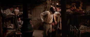Movie still from “The Cowboys” (1972), directed by Mark Rydell – A man standing in front of another man in front of a fireplace; Medium shot, Over the shoulder angle