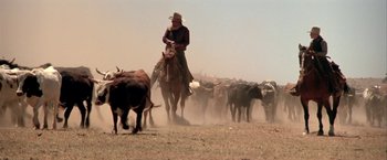 Movie still from “The Cowboys” (1972), directed by Mark Rydell – A man on a horse herds a herd of cattle; Wide shot, Low angle