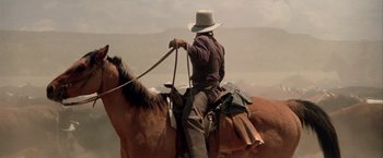 Movie still from “The Cowboys” (1972), directed by Mark Rydell – A man riding on the back of a brown horse; Medium shot, Low angle