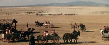 Movie still from “The Cowboys” (1972), directed by Mark Rydell – A group of people riding on the back of a horse drawn carriage; Extreme Wide shot, High angle