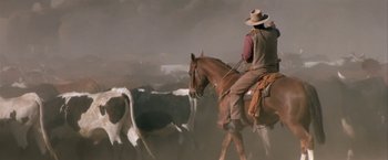Movie still from “The Cowboys” (1972), directed by Mark Rydell – A man on a horse herds a herd of cattle; Wide shot, Low angle