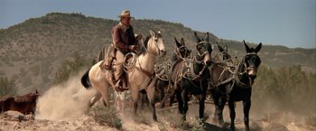 Movie still from “The Cowboys” (1972), directed by Mark Rydell – A man riding on the back of a white horse; Wide shot, Low angle