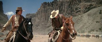 Movie still from “The Cowboys” (1972), directed by Mark Rydell – A man riding on the back of a brown horse; Wide shot, Low angle