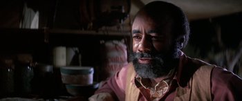 Movie still from “The Cowboys” (1972), directed by Mark Rydell – A man with a goatee and beard sitting at a table; Close Up shot, Low angle