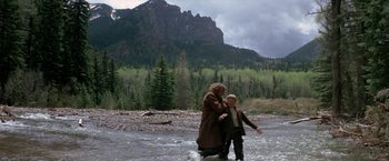 Movie still from “The Cowboys” (1972), directed by Mark Rydell – A man and a woman walking across a river; Wide shot, Low angle
