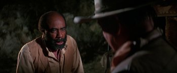 Movie still from “The Cowboys” (1972), directed by Mark Rydell – A man with a beard is talking to another man in a cowboy hat; Close Up shot, Over the shoulder angle