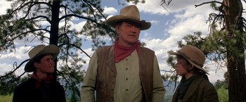 Movie still from “The Cowboys” (1972), directed by Mark Rydell – An older man wearing a cowboy hat standing next to a tree; Medium shot, Low angle