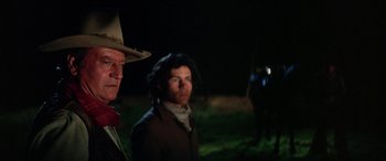 Movie still from “The Cowboys” (1972), directed by Mark Rydell – A man in a cowboy hat standing next to another man; Medium shot, Over the shoulder angle