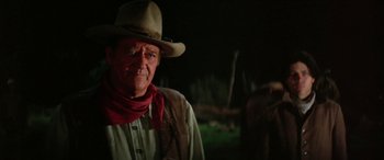 Movie still from “The Cowboys” (1972), directed by Mark Rydell – An older man wearing a cowboy hat with a horse in the background; Medium shot, Over the shoulder angle