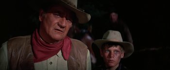 Movie still from “The Cowboys” (1972), directed by Mark Rydell – A man and a boy wearing cowboy hats and bandannas; Close Up shot, Over the shoulder angle