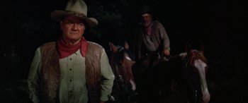 Movie still from “The Cowboys” (1972), directed by Mark Rydell – A man in a cowboy hat standing next to another man on a horse; Medium shot, Low angle