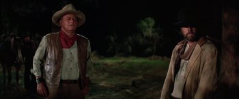 Movie still from “The Cowboys” (1972), directed by Mark Rydell – A man in a cowboy hat standing next to another man in a cowboy hat; Medium shot, Over the shoulder angle