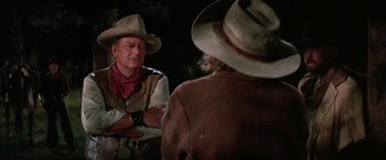Movie still from “The Cowboys” (1972), directed by Mark Rydell – A man in a cowboy hat talking to another man in a cowboy hat; Medium shot, Over the shoulder angle