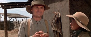 Movie still from “The Cowboys” (1972), directed by Mark Rydell – A man wearing a hat standing in front of a wall; Close Up shot, Low angle