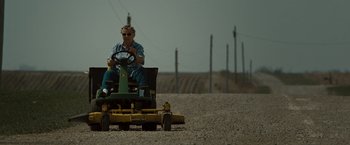 Movie still from “The Crazies” (2010), directed by Breck Eisner – A man riding a lawn mower on top of a dirt field; Wide shot, Low angle
