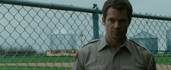 Movie still from “The Crazies” (2010), directed by Breck Eisner – A man standing in front of a chain link fence; Close Up shot, Over the shoulder angle
