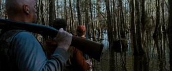 Movie still from “The Crazies” (2010), directed by Breck Eisner – A man is holding a rifle in the water; Medium shot, High angle