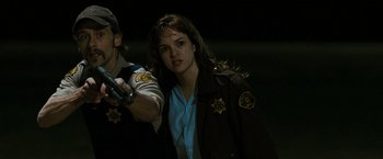 Movie still from “The Crazies” (2010), directed by Breck Eisner – A woman in a brown jacket holding a gun; Medium shot, Over the shoulder angle