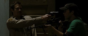 Movie still from “The Crazies” (2010), directed by Breck Eisner – A man holding a gun in his hand while another man holds a gun in his other hand; Medium shot, Over the shoulder angle