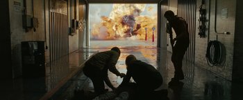 Movie still from “The Crazies” (2010), directed by Breck Eisner – Two people kneeling down in front of an image of an explosion; Wide shot, Over the shoulder angle