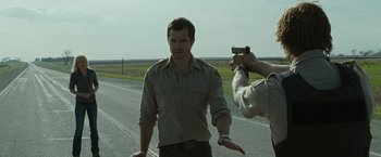Movie still from “The Crazies” (2010), directed by Breck Eisner – A man is being filmed by a police officer on the side of the road; Medium shot, Over the shoulder angle