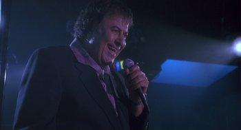Movie still from “The Crossing Guard” (1995), directed by Sean Penn – A man in a black jacket is singing into a microphone; Close Up shot, Low angle