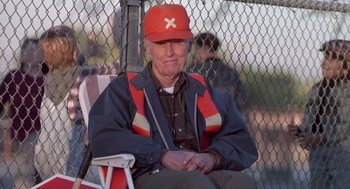 Movie still from “The Crossing Guard” (1995), directed by Sean Penn – An older man sitting in a chair wearing an orange baseball cap; Medium shot, Low angle