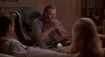 Movie still from “The Crossing Guard” (1995), directed by Sean Penn – A man sitting in a chair in front of a candle; Medium shot, Over the shoulder angle