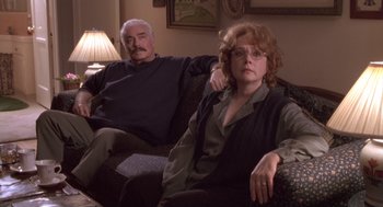 Movie still from “The Crossing Guard” (1995), directed by Sean Penn – A man and a woman sitting on a couch in a living room; Medium shot, High angle