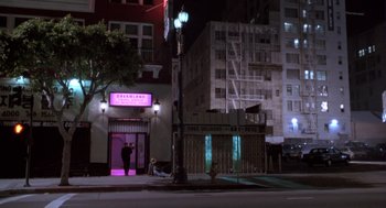 Movie still from “The Crossing Guard” (1995), directed by Sean Penn – A man standing on the sidewalk in front of a building at night; Wide shot, High angle