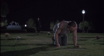 Movie still from “The Crossing Guard” (1995), directed by Sean Penn – A man in grey tank top on grass at night; Wide shot, High angle