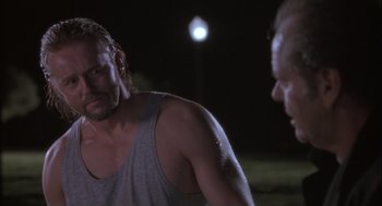 Movie still from “The Crossing Guard” (1995), directed by Sean Penn – A man standing next to another man on a field; Close Up shot, Over the shoulder angle