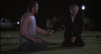 Movie still from “The Crossing Guard” (1995), directed by Sean Penn – Two men sitting on the grass shaking hands; Medium shot, Over the shoulder angle
