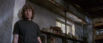 Movie still from “The Crying Game” (1992), directed by Neil Jordan – A young man standing in a room with shelves of pots; Medium shot, Low angle