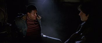 Movie still from “The Crying Game” (1992), directed by Neil Jordan – A man sitting on the ground talking on a cell phone; Medium shot, High angle