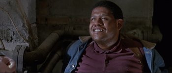 Movie still from “The Crying Game” (1992), directed by Neil Jordan – A person sitting in a chair smiling; Close Up shot, Low angle