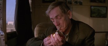 Movie still from “The Crying Game” (1992), directed by Neil Jordan – An older man smoking a cigarette with a lit cigarette in his mouth; Close Up shot, Low angle