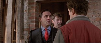 Movie still from “The Crying Game” (1992), directed by Neil Jordan – A man wearing a suit and tie standing next to two other men; Close Up shot, Over the shoulder angle