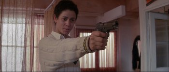 Movie still from “The Crying Game” (1992), directed by Neil Jordan – A man in a sweater holding a gun in a room; Medium shot, Low angle