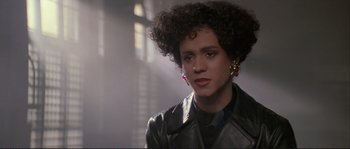 Movie still from “The Crying Game” (1992), directed by Neil Jordan – A woman in a black leather jacket and red earrings looks at the camera; Close Up shot, Over the shoulder angle