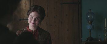 Movie still from “The Current War: Director's Cut” (2017), directed by Alfonso Gomez-Rejon – A woman smiling in front of a wooden wall; Close Up shot, Over the shoulder angle