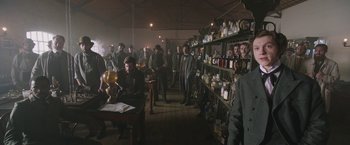 Movie still from “The Current War: Director's Cut” (2017), directed by Alfonso Gomez-Rejon – A group of people standing in a room with many jars; Wide shot, Low angle