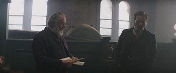 Movie still from “The Current War: Director's Cut” (2017), directed by Alfonso Gomez-Rejon – A man with a beard is holding a book; Medium shot, Low angle