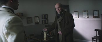 Movie still from “The Current War: Director's Cut” (2017), directed by Alfonso Gomez-Rejon – A bald man in a suit and tie holding an object in his hand; Medium shot, Low angle