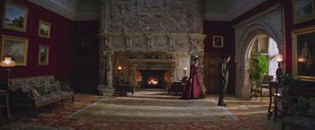 Movie still from “The Current War: Director's Cut” (2017), directed by Alfonso Gomez-Rejon – A woman in a red dress standing in front of a fireplace; Extreme Wide shot, High angle