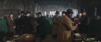 Movie still from “The Current War: Director's Cut” (2017), directed by Alfonso Gomez-Rejon – A group of men standing around in a room; Wide shot, Low angle